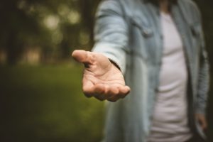Young man in standing in park stretches his hand. Focus is on hand. Close up.