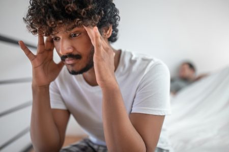 Sad Indian man sitting on the bed with his hands on the temples and back turned to his companion